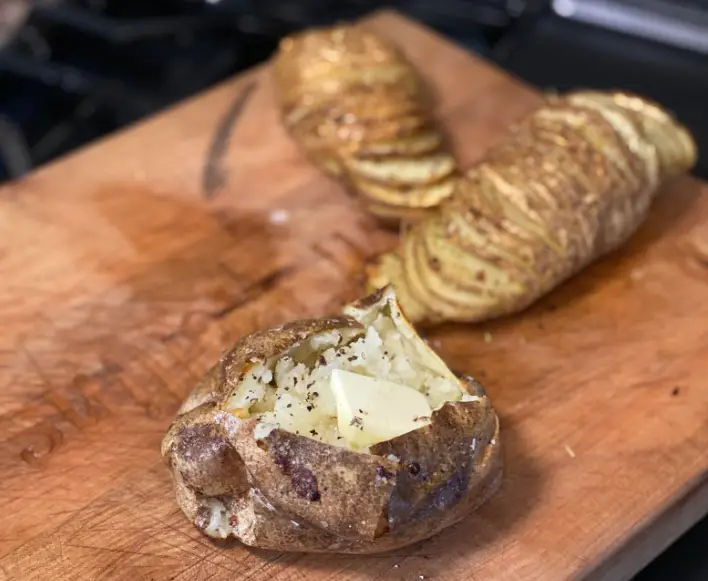 Baked potatoes with butter on wooden board.