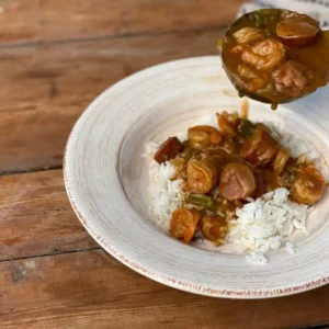 A bowl of rice and stew with sauce on top.