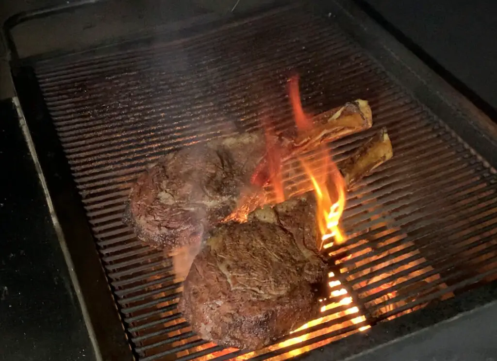 A grill with some meat on it and flames coming out of the grill.