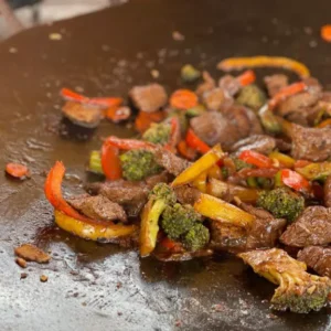 A wok with meat and vegetables on it.