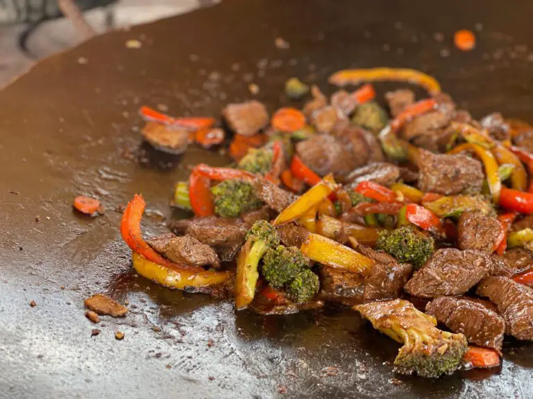 A wok with meat and vegetables on it.