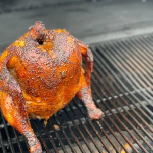 A chicken is sitting on the grill grate.