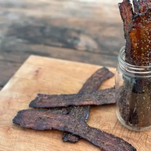 A jar of jerky sitting next to some other food.