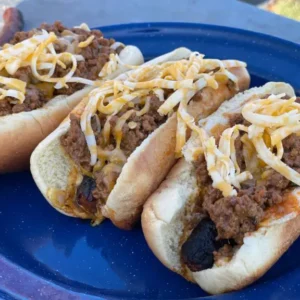 Three chili cheese dogs on a blue plate.