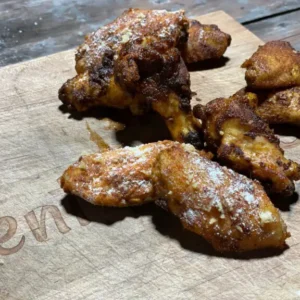 A wooden cutting board with some chicken wings on it