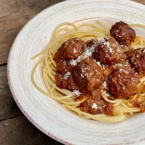 A white plate topped with spaghetti and meatballs covered in sauce.