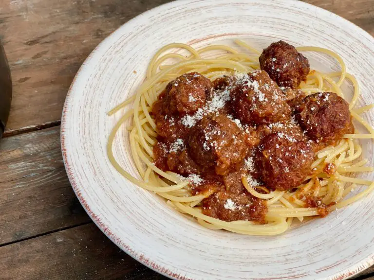 A white plate topped with spaghetti and meatballs covered in sauce.