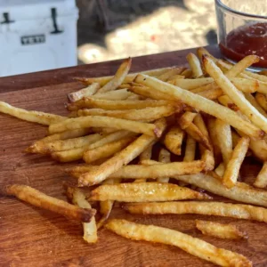 A pile of french fries on top of a wooden board.