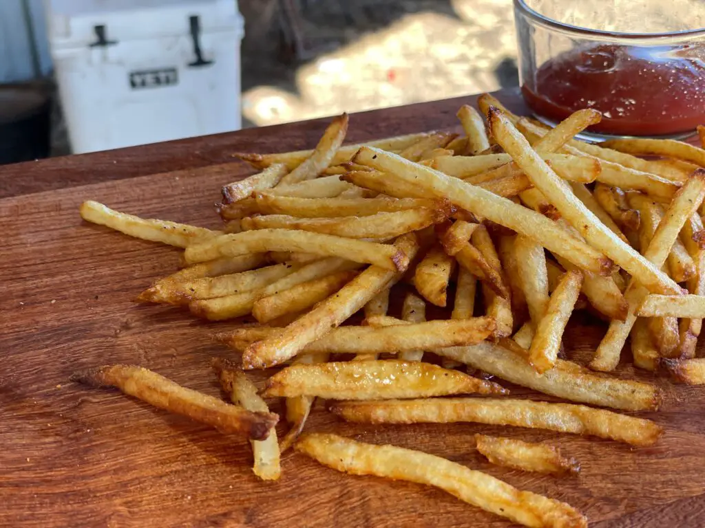 A pile of french fries on top of a wooden board.