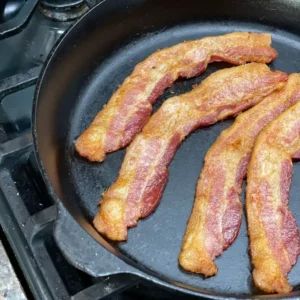 A pan with bacon in it on top of the stove.