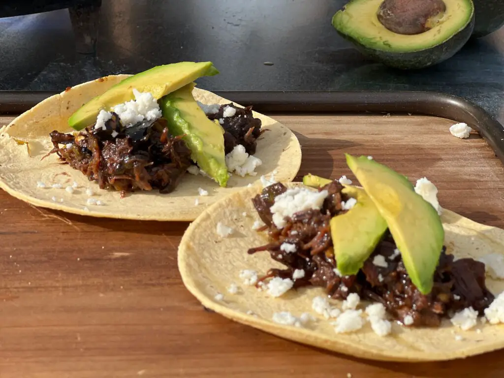Close up photo of two barbacoa tacos topped with avocado 
