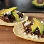 Close up photo of two barbacoa tacos topped with avocado