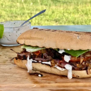 Grilled steak sandwich with sauce and lettuce.