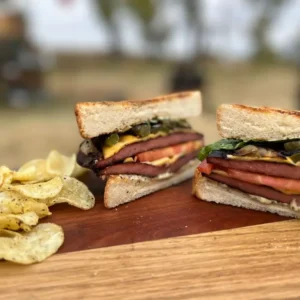 Two grilled sandwiches with chips on a wooden board.