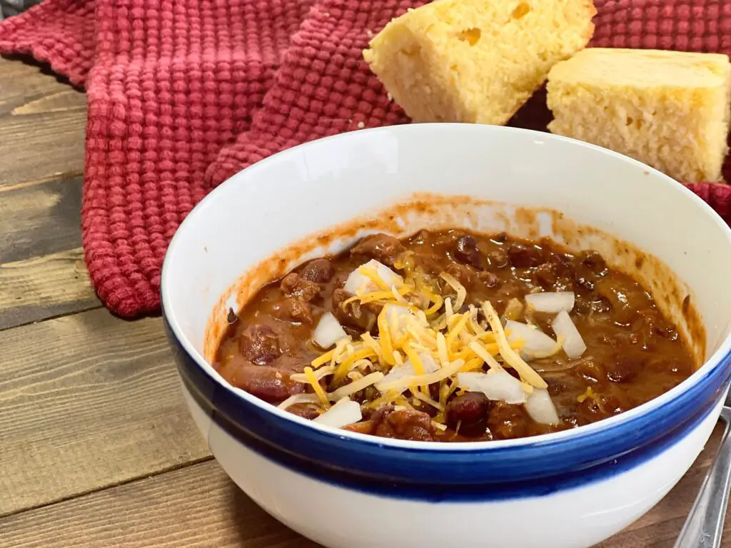 A bowl of chili with cheese and onions.