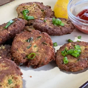 A plate of crab cakes with lemon and ketchup.