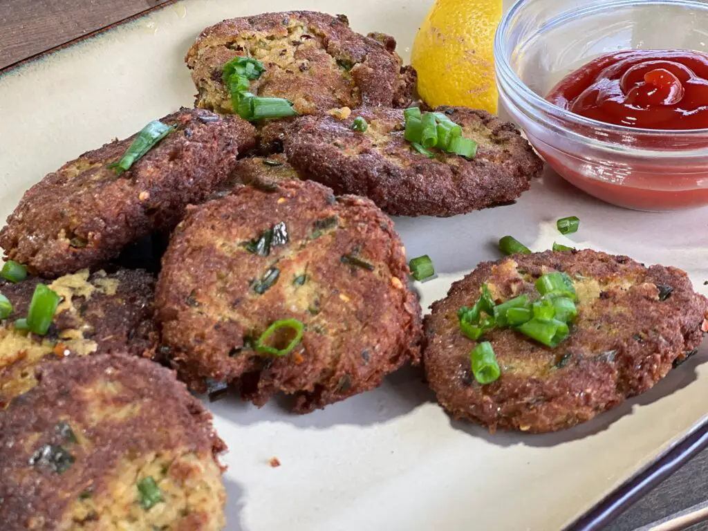 A plate of crab cakes with lemon and ketchup.