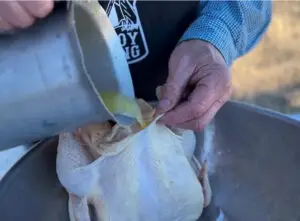 Kent Rollins is holding the outer skin of the chicken away from the breast meat, and pouring the olive oil/wine mixture inside the skin. 