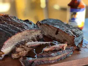A delicious smoked brisket with a dark brown crust is smoked to perfection, slicked thick, and drizzled with Red River Mud BBQ Sauce by Kent Rollins,