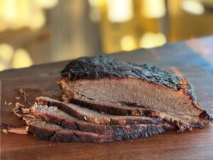 a perfectly smoked brisket is sliced on a mesquite wood cutting board.