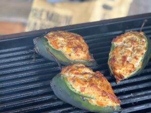 Three stuffed poblano peppers in a haze of smoke from the grill