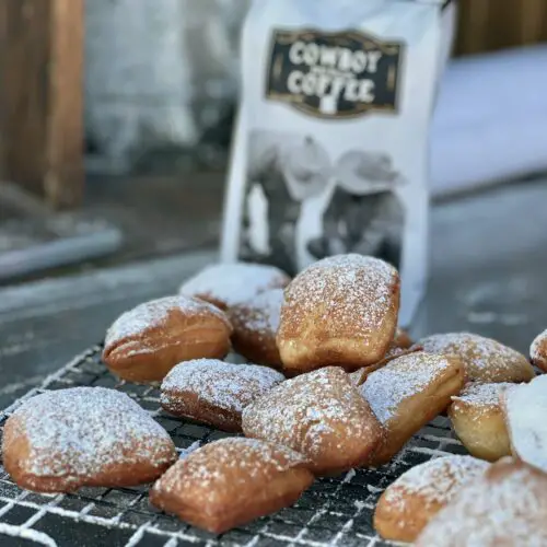 A photo of Kent Rollin's Cowboy Coffee next to a wire rack covered in golden beignets covered with powdered sugar.
