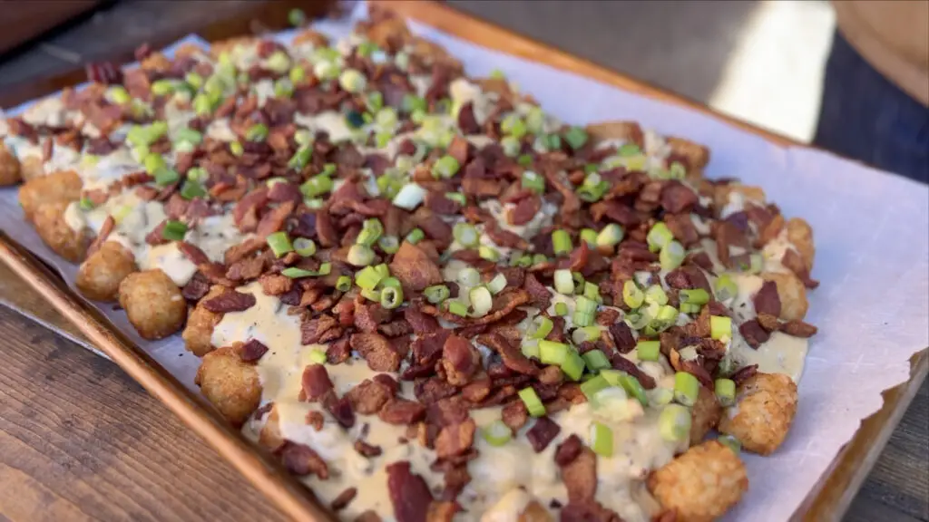 A sheet pan of loaded tater tots. Crispy fried tater tots covered in cheese sauce with brisket, crispy bacon, and green onions all over.