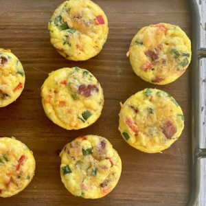 A tray of mini quiches with ham and peppers.