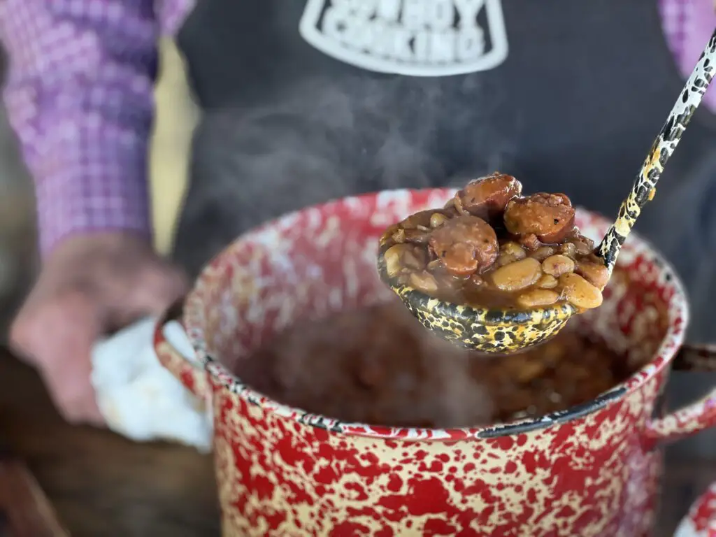Kent Rollins lifts a ladle full of delicious smoked sausage and beans.