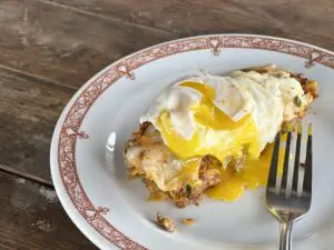 A white plate with red trim holds an enchilada covered with a sunny side up egg