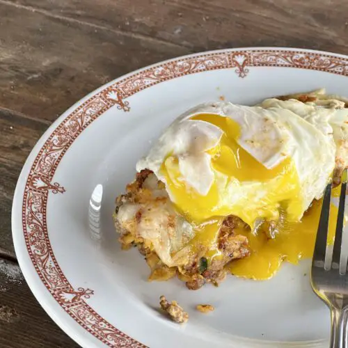 A white plate with red trim holds an enchilada covered with a sunny side up egg