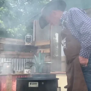 Man in a hat smoking food outdoors.