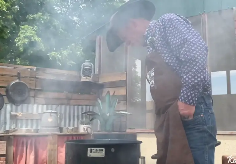 Man in a hat smoking food outdoors.