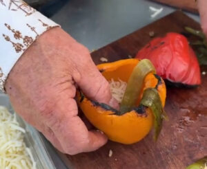 Kent Rollins holds a yellow bell pepper with strips of smoked anaheim peppers draped over the sides.