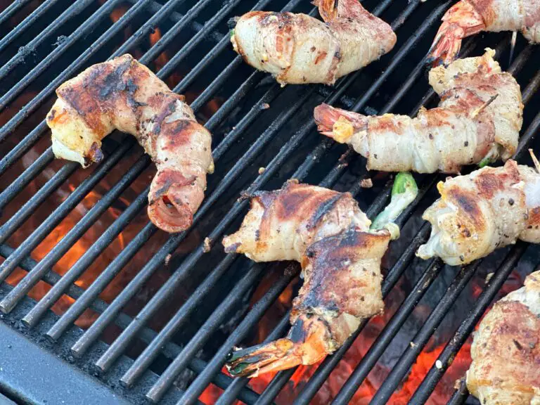 Grilled bacon wrapped stuffed shrimp on a gril with fire peeking through the grates