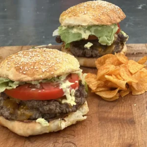 Two cheeseburgers with lettuce and tomato on a wooden board.