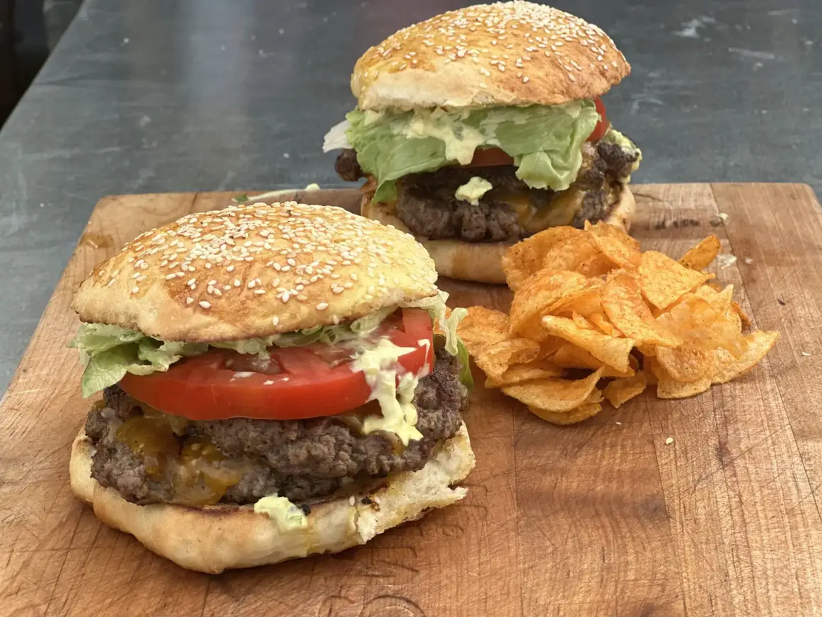 Two cheeseburgers with lettuce and tomato on a wooden board.