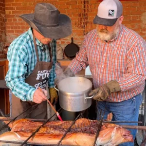 Two men cooking fish on a grill.