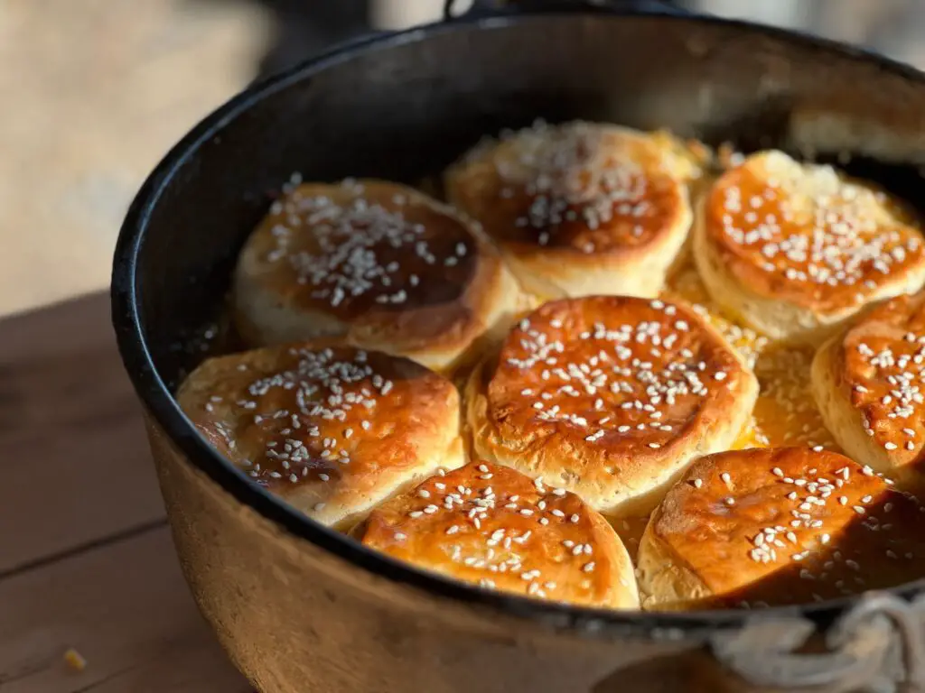 A circle of 7 browned biscuits sprinkled with sesame seeds - one biscuit in the middle - in a dutch oven.