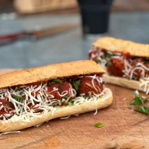 A meatball sandwich with cheese and herbs on top.