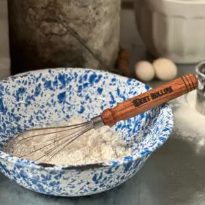 A blue and white bowl with flour and a whisk.