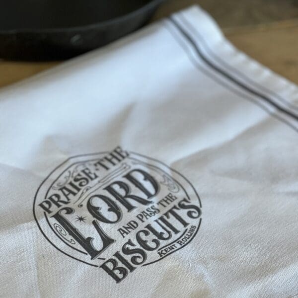 White tea towel with "Praise the Lord and pass the biscuits" design.