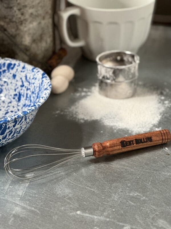 Wooden handled whisk on a counter.