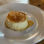 A white plate topped with a cheesecake covered in caramel.