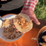 A person holding a tortilla over some food.