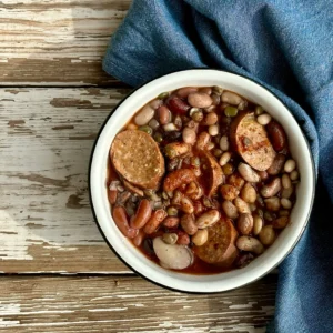 A bowl of beans and sausage on top of a table.