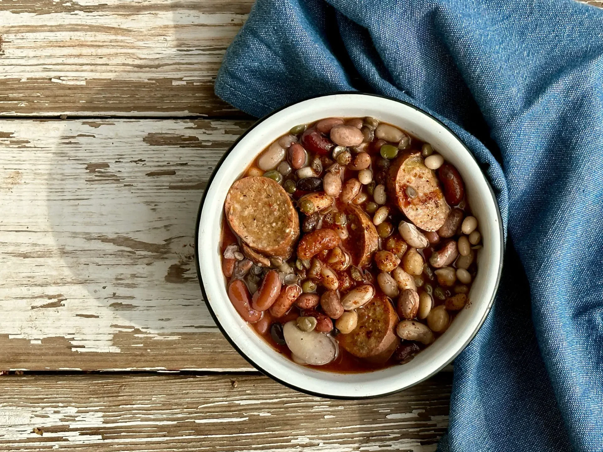 A bowl of beans and sausage on top of a table.