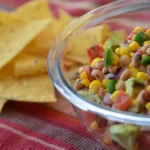 A bowl of beans and corn next to tortilla chips.