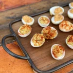 A tray of deviled eggs with cheese on top.