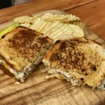 A toasted sandwich cut in half on top of a wooden board.